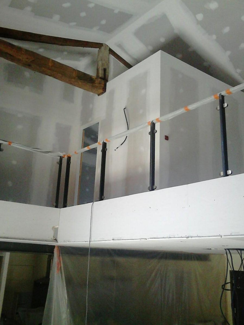 Chantier de rénovation : mezzanine avec garde-corps temporaire en tubes plastiques, murs et plafond en plaques de plâtre non peintes, poutre en bois apparente.