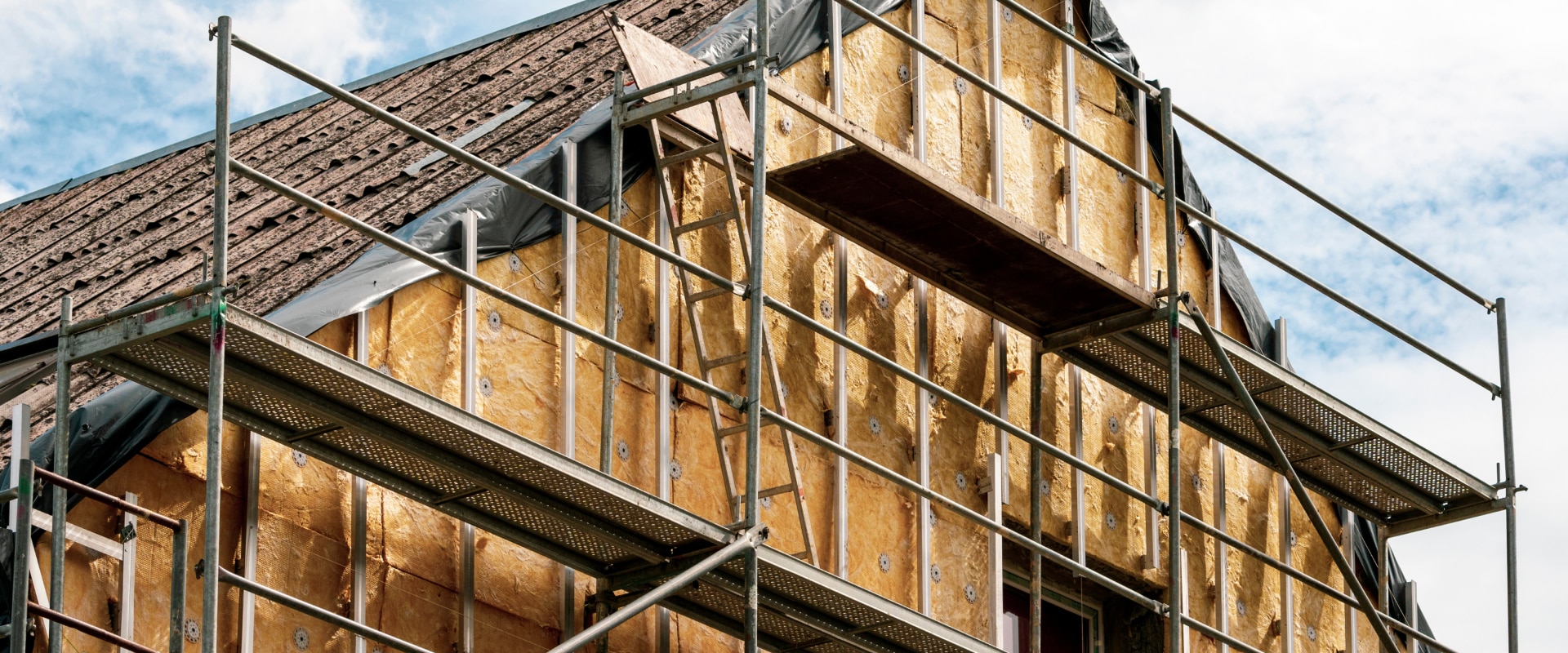 Chantier de rénovation : échafaudage devant une façade en cours d'isolation thermique avec laine minérale jaune.