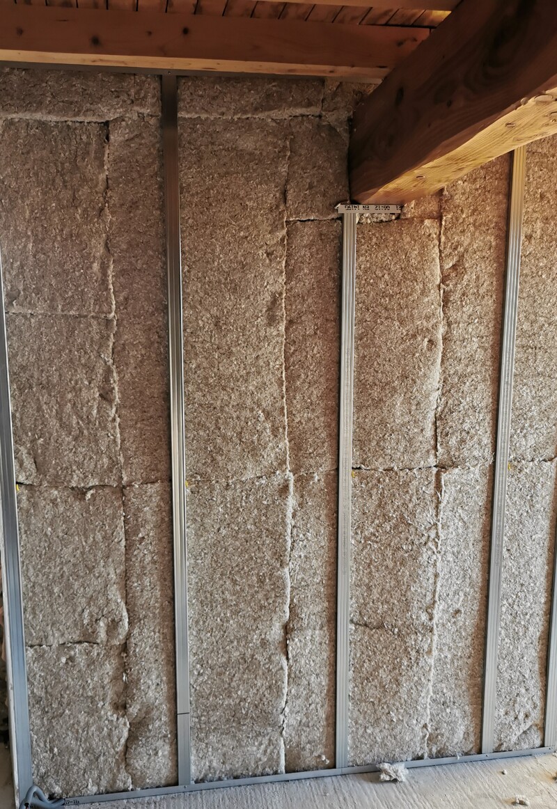 Isolation thermique en laine minérale entre montants métalliques pour cloison, avec poutre en bois visible en haut. Texte visible sur montant : 06.12 21.00.